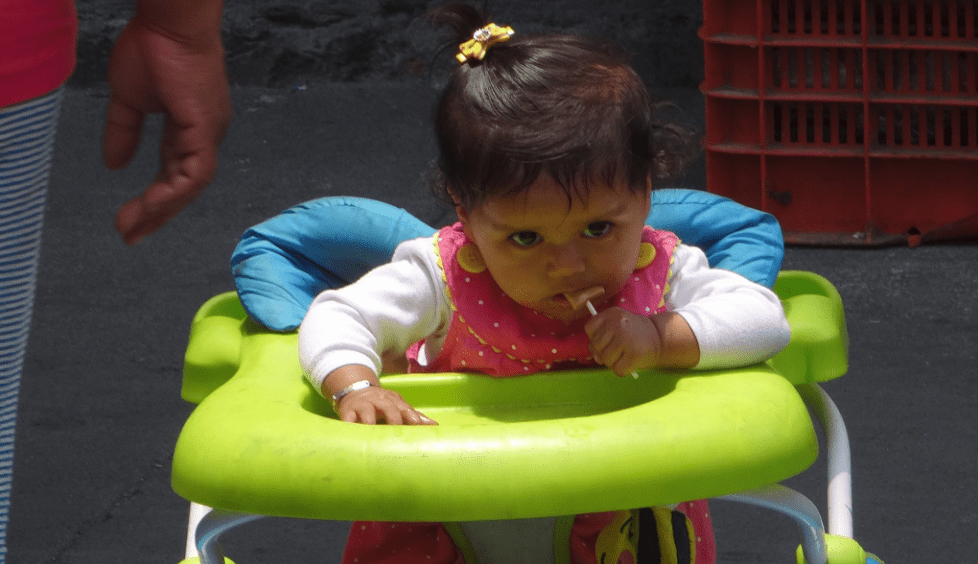 best baby walker: a small child sucks on a piece of candy while sitting in a training walker