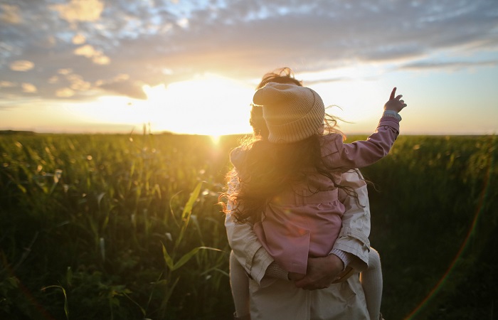 woman holding girl set against a sunset over a field