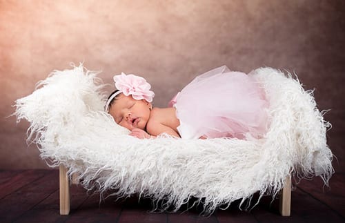baby wearing pink dress sleeping on a crib