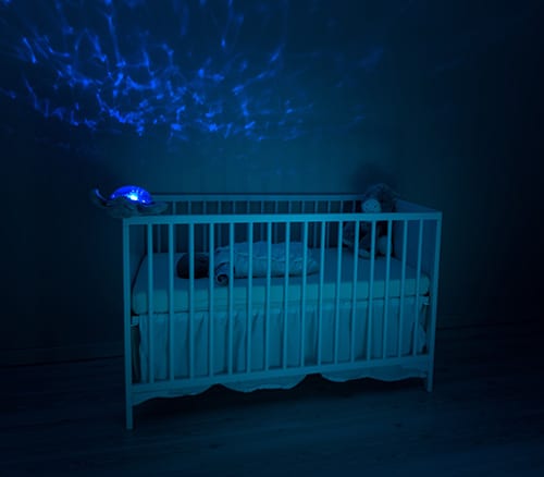 sleeping baby on a white crib with blue light in a dark room