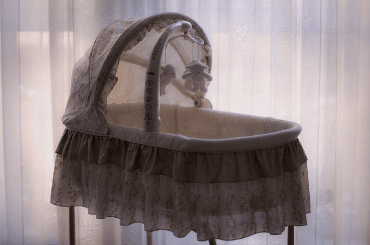 infant bed with hanging stuffed toy against white curtain